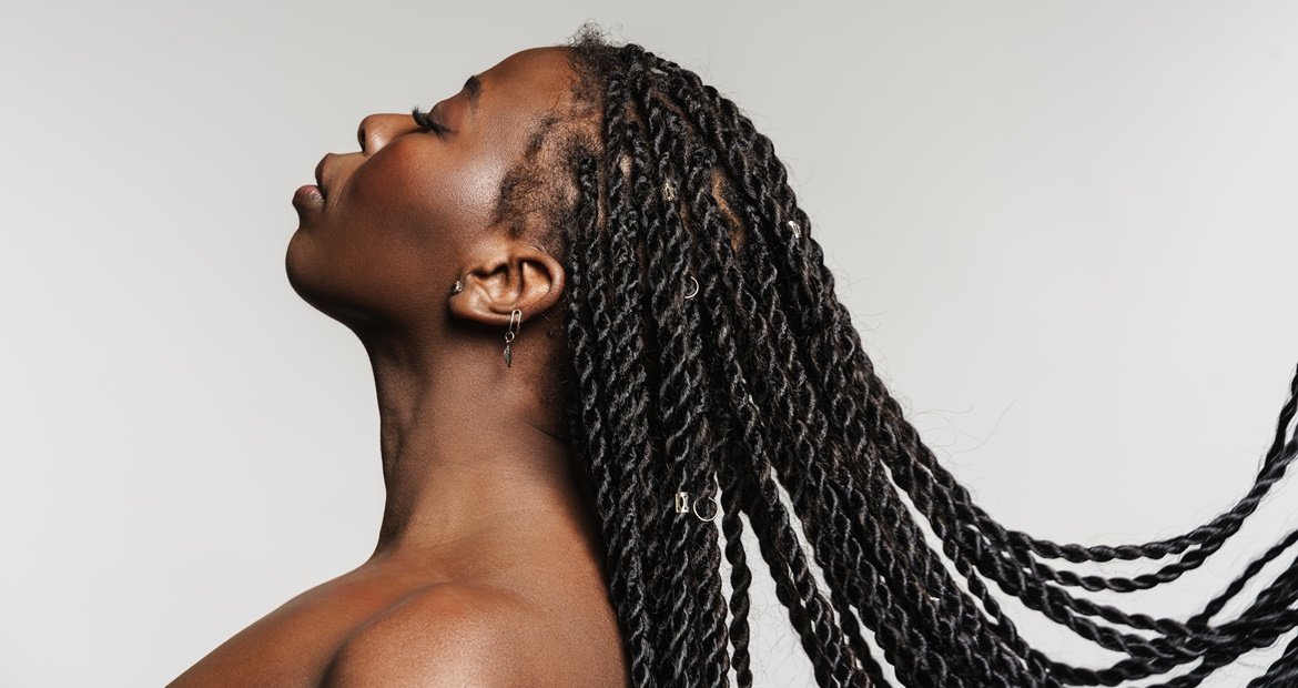 Mulher negra olhando para o lado com as tranças soltas ao vento em um fundo branco.